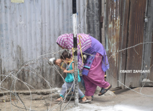 Woman with child crossing razor wire barrier (Basit Zargar) July 8 2017